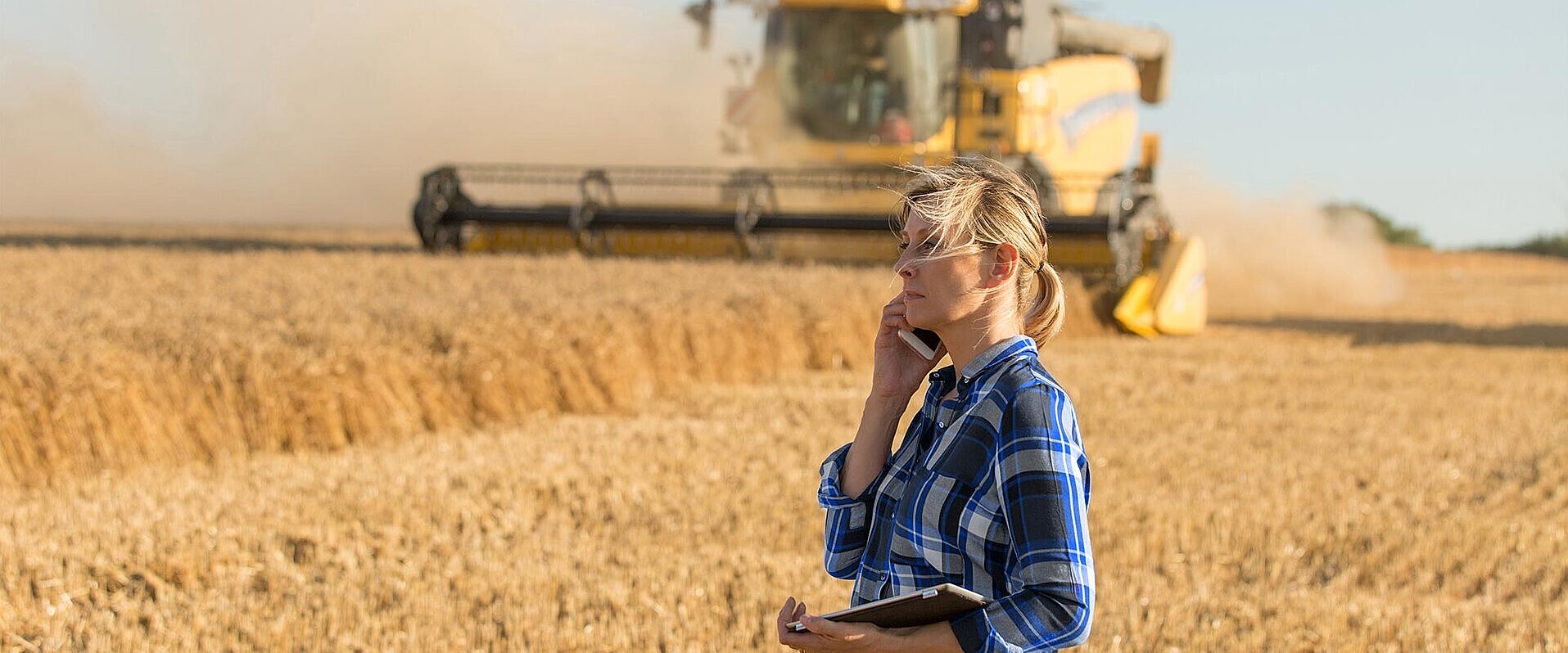 Eine Landwirtin steht auf einem Feld vor einem Mähdräscher.