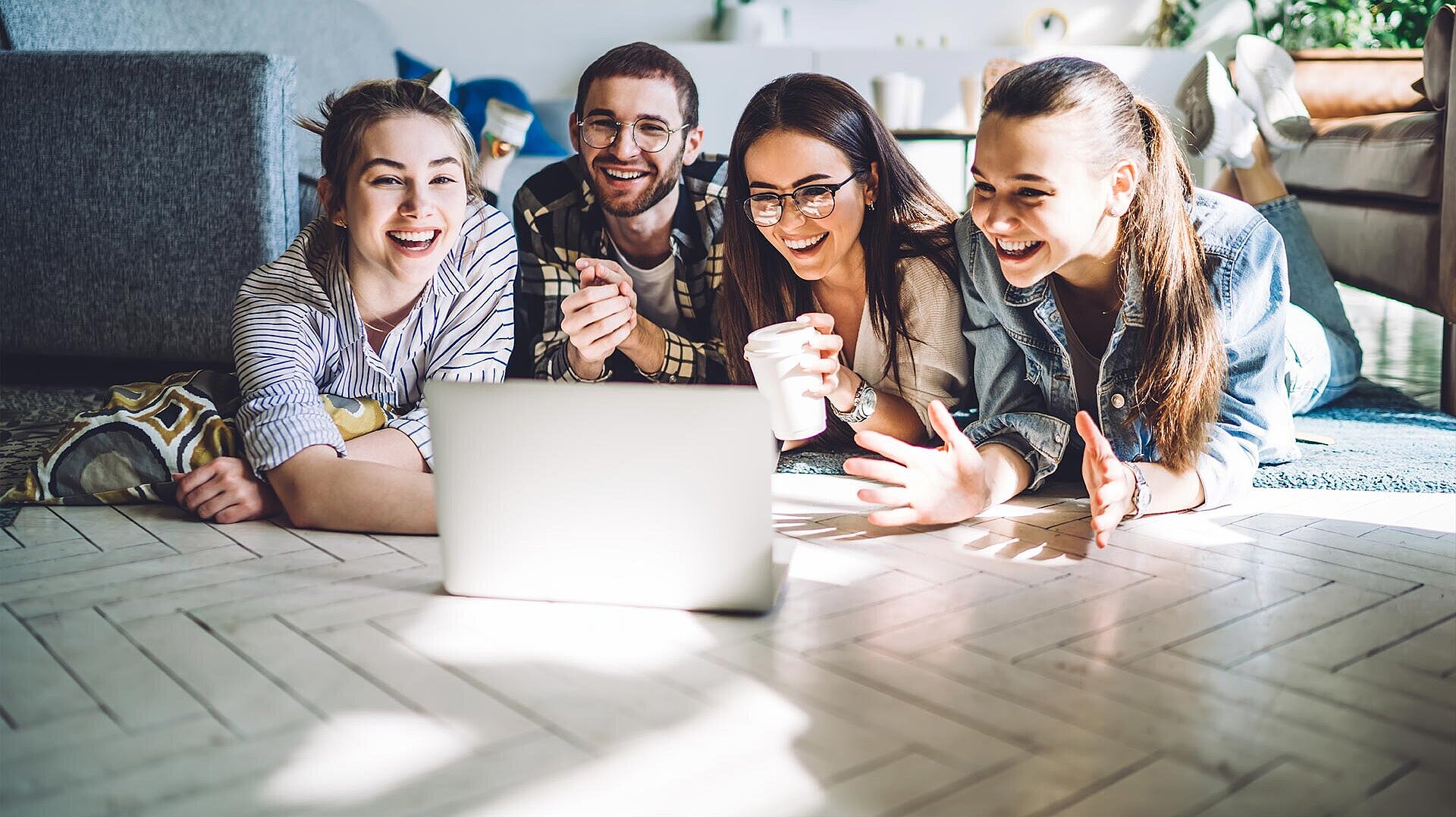 Ein Mann und drei Frauen liegen auf dem Fußboden und gucken zusammen auf einen Laptop