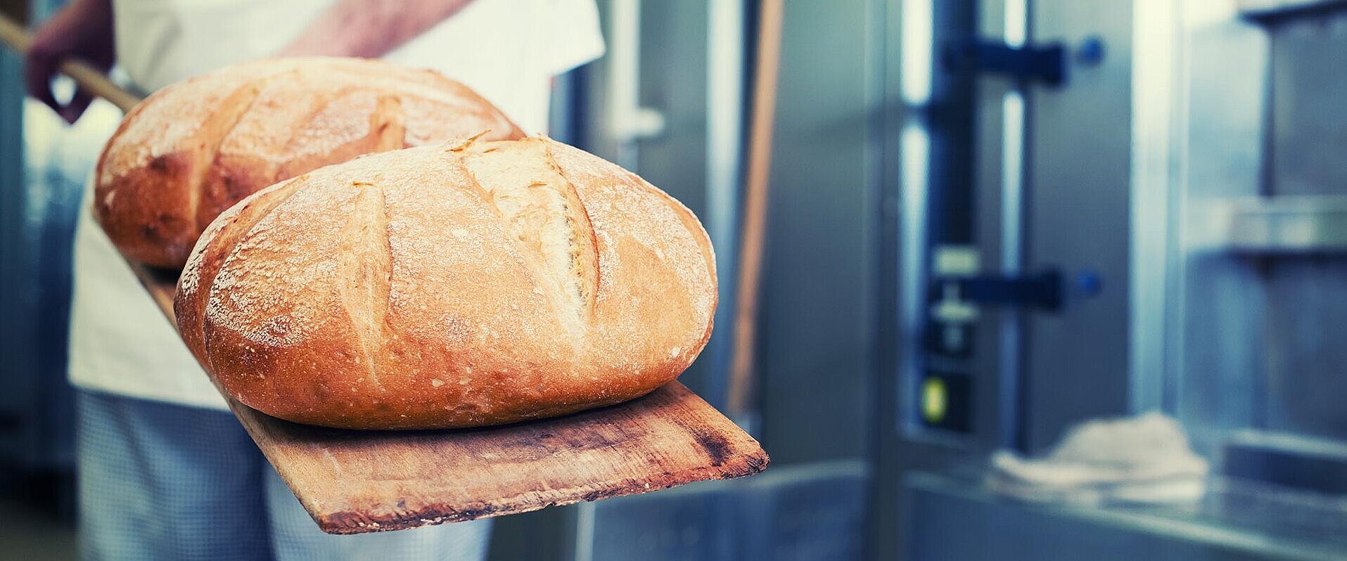 Ein Bäcker als Gewerbekunde, der sein frisches Brot aus dem Ofen holt.