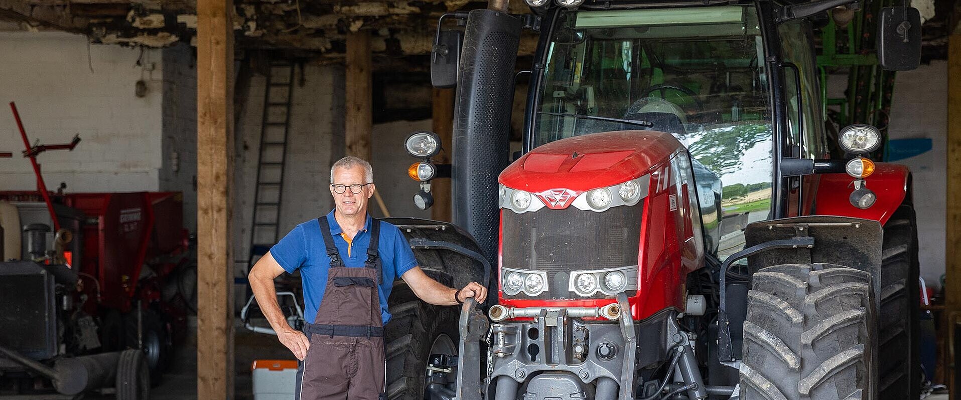 Roter Traktor in einer Scheune mit einem Landwirt im Vordergrund.