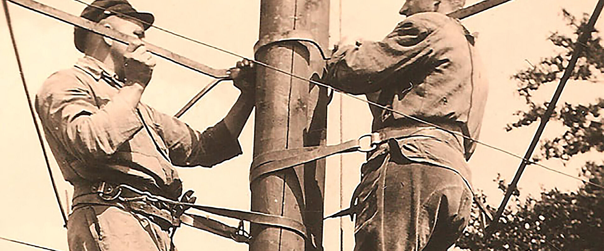 Sepia-Aufnahme zweier Monteure auf einem Strommast.